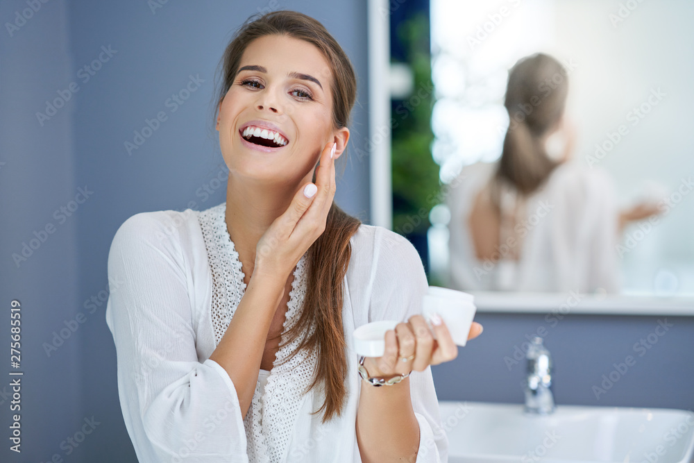 Beautiful brunette woman applying face cream in the bathroom - obrazy, fototapety, plakaty 
