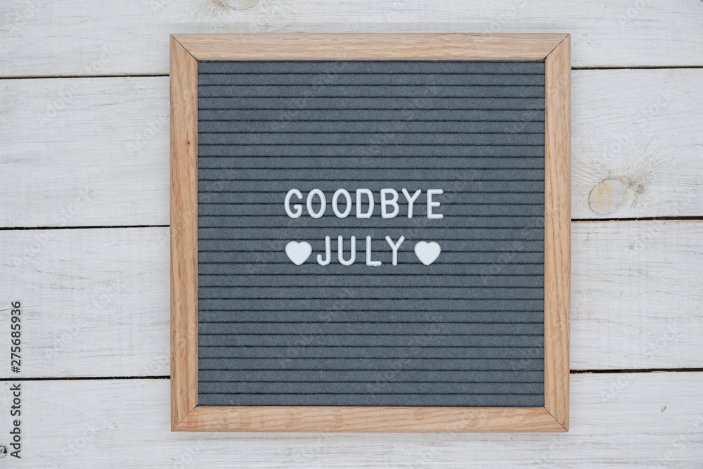 text in English goodbye July and a heart sign on a gray felt Board in a wooden frame