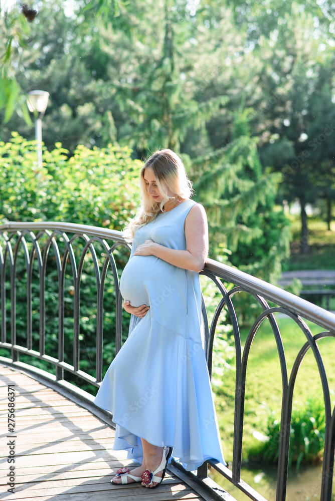 Naklejka premium Beautiful portrait of a pregnant woman on a warm summer day in the nature. Pregnancy and season concept