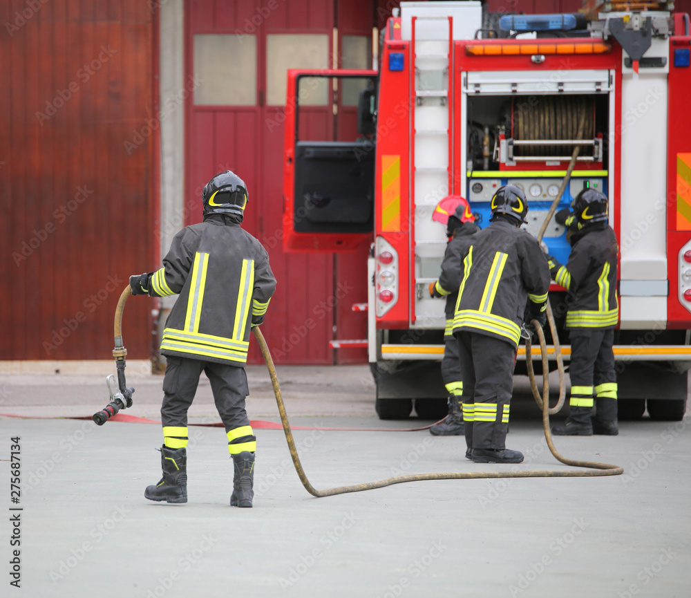 three firefighters in action and the fire engine with hose - obrazy, fototapety, plakaty 