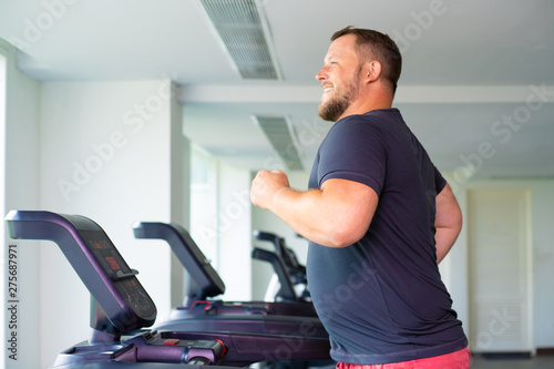 chubby man walking on running track, warming up on gym treadmill.