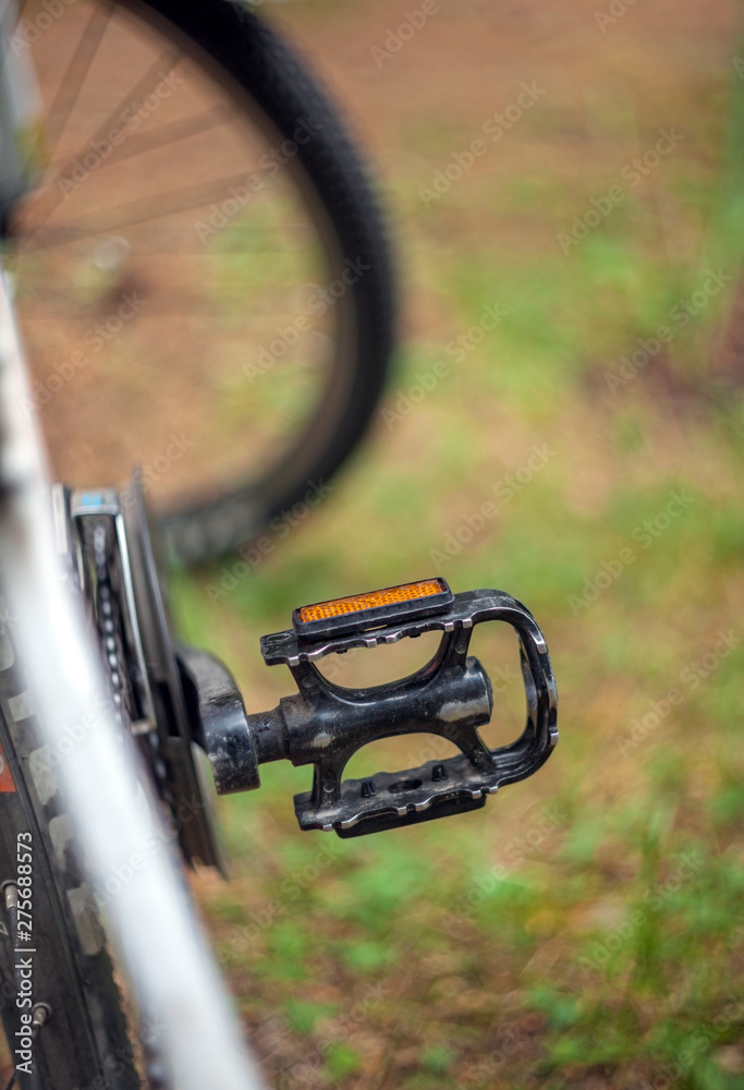Shabby bicycle pedal on a blurred background of the wheel and grass. Shabby bicycle pedal on a blurred background of the wheel and grass.