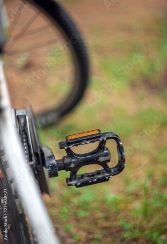 Shabby bicycle pedal on a blurred background of the wheel and grass.