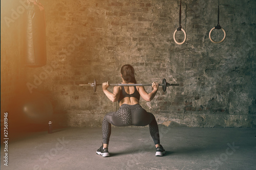 Girl in black sportswear doing squats with barbell. Strength and motivation concept