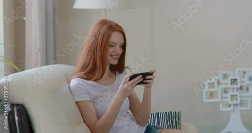 attractive girl sitting at home on the couch playing a game on a smartphone. in slow motion. Shot on Canon 1DX mark2 4K camera photo