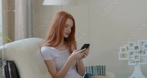 attractive girl sitting at home on the couch  typing a message on the smartphone. in slow motion. Shot on Canon 1DX mark2 4K camera photo