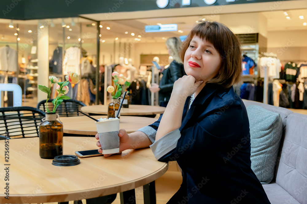 ordinary middle-aged woman sitting in a cafe in the Mall and thoughtfully drinking coffee