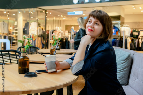 ordinary middle-aged woman sitting in a cafe in the Mall and thoughtfully drinking coffee