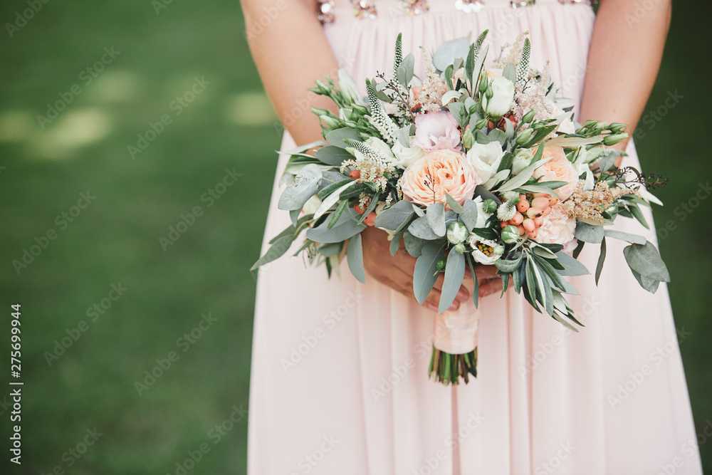 The bride in an elegant wedding dress holds a beautiful bouquet of different flowers and green leaves. Wedding theme