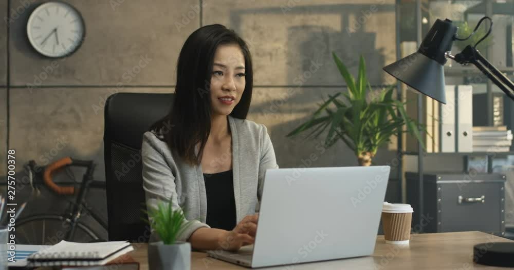 Young Asian attractive female office worker sitting at the laptop computer at the desk, working and thinking.