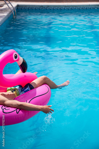 Young man floating in a inflatable flamingo in a blue pool a sunny day of summer vacation