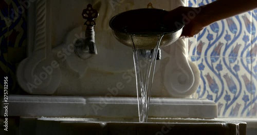 human is pouring water from bronze cup into stone washbasin in dark room, close-up