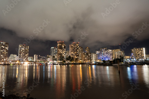 Honolulu night cityscape with lights reflected in water on a cloudy night