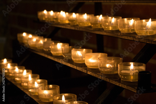 Row of glowing candles in church. Candles with flame on dark background. Faith and religion concept. Candles in catholic church. Peace and hope concept. Candlelight background. Church interior. 