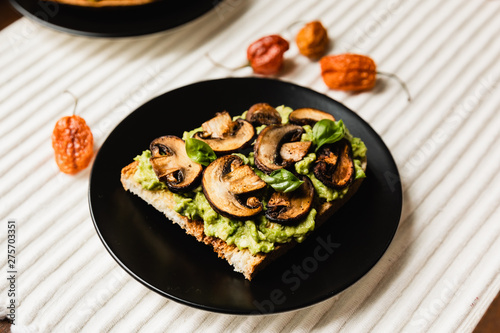 Avocado Toast with Mushrooms On A Black Plate with Light Background