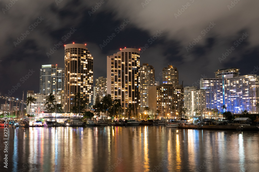 Honolulu night cityscape with lights reflected in water on a cloudy night