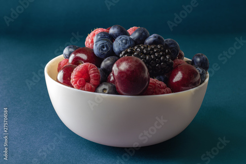 Ripe juicy berries in a white plate, raspberries, cherries, blackberries, blueberries. A useful berry for the body