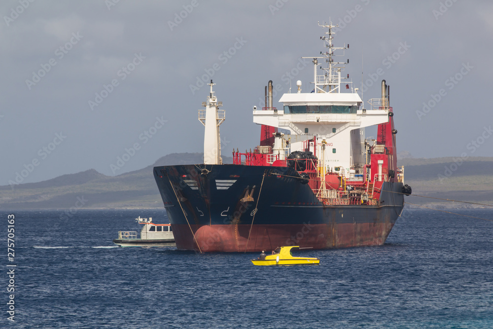 Cargo ship getting in anchoring position by a tugboat for making a delivery of industry parts in shallow water on the west coast of the tropical island of Bonaire