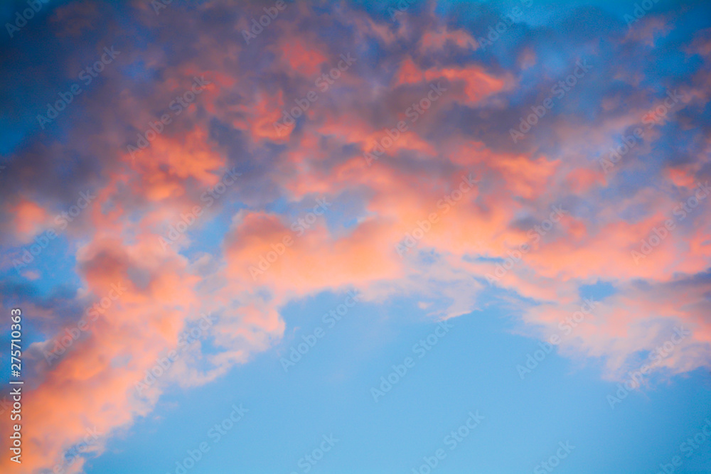 The clouds in the blue sky are illuminated by the orange setting sun. Natural background.