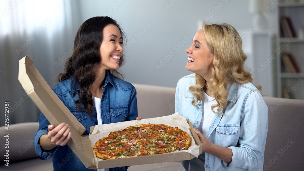 Cheerful women with huge pizza laughing and having fun at home, fast food