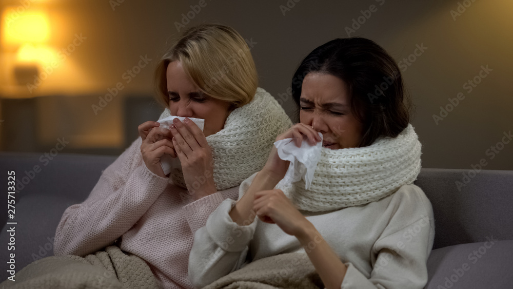 Young students in scarfs sneezing in tissue, suffering flu, winter epidemic