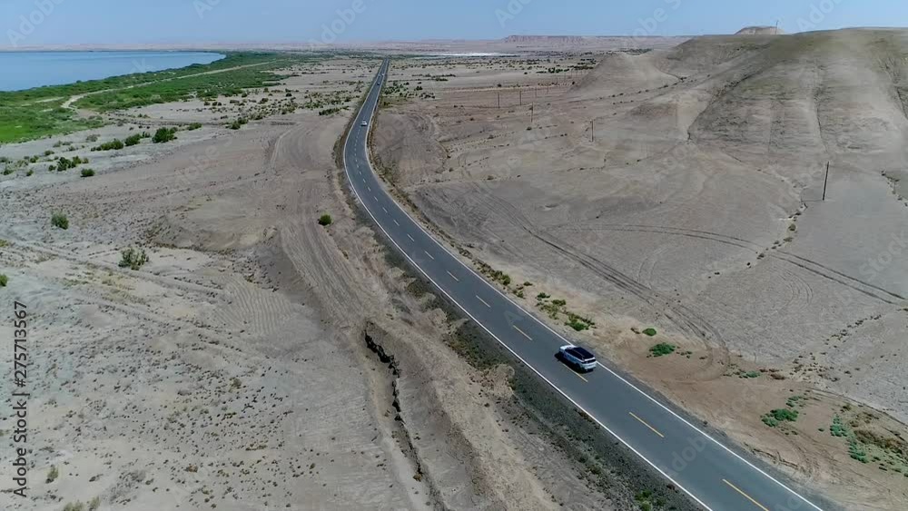 Aerial view of cars driving on en empty road in the middle of the desert next The Ailik or Aylik lake in Xinjiang Uighur Autonomous Region of China. Aerial view of cars driving on en empty road in the middle of the desert next The Ailik or Aylik lake in Xinjiang Uighur Autonomous Region of China.
