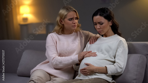 Woman supporting her upset pregnant friend, holding hand, single future mother