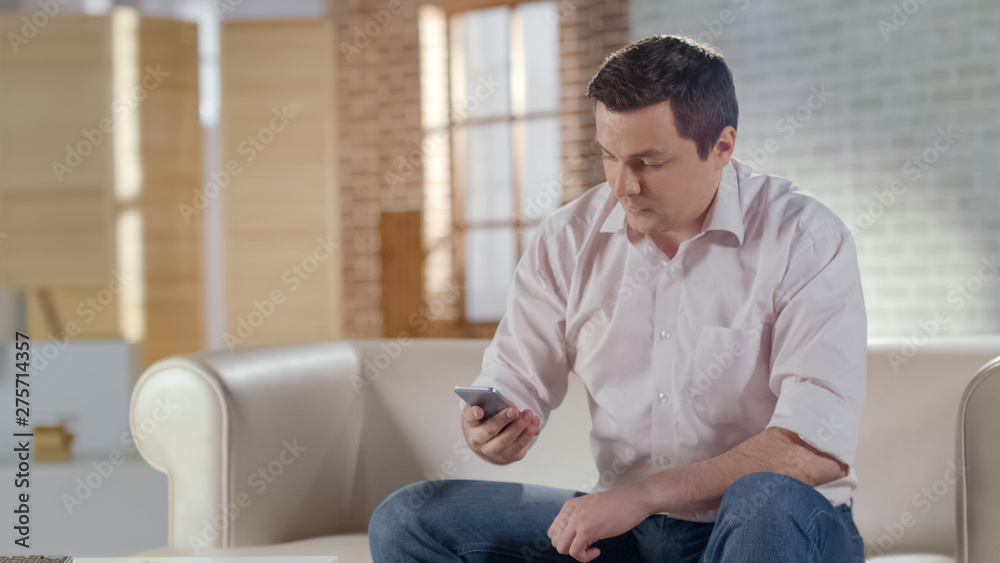 Young man dialing number or reading message from business partner on phone