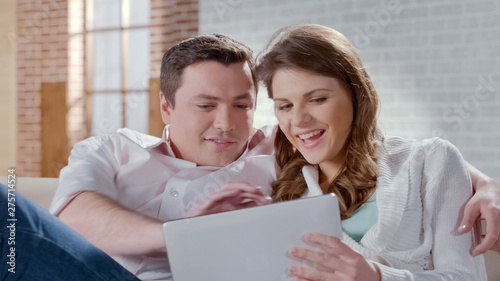 Happy young couple viewing photos on tablet, choosing items in online shop