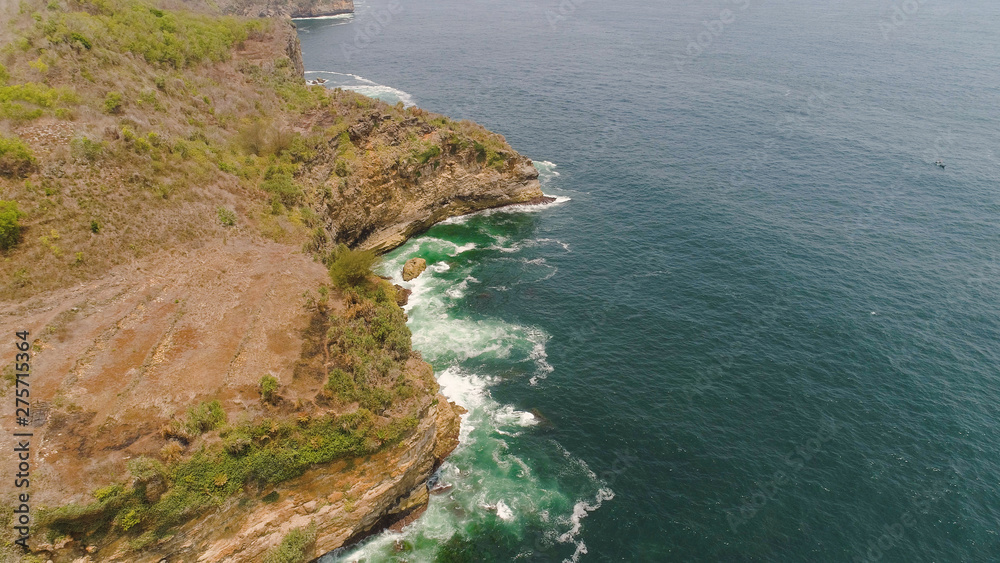 aerial view rocky coastline with cliffs, ocean surf with breaking waves in coast. seascape waves break on rocky shore java, indonesia