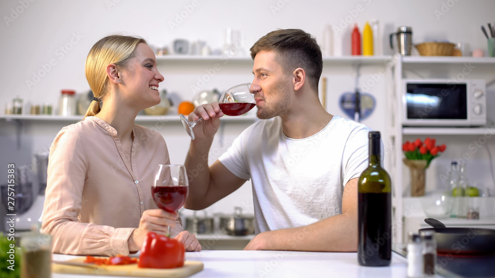 Young couple drinking wine in kitchen, chatting and relaxing together, romance Young couple drinking wine in kitchen, chatting and relaxing together, romance