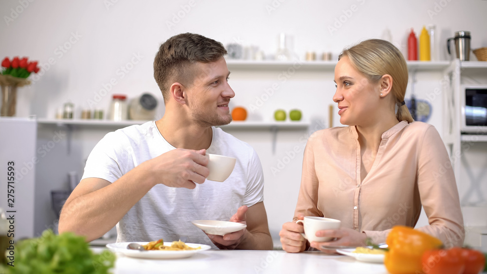 Loving couple communicating at kitchen, holding coffee cup, time together