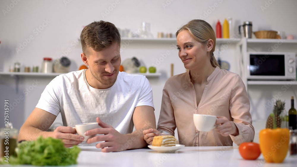 Cheerful man and woman having tea time with sweet cake at kitchen, togetherness