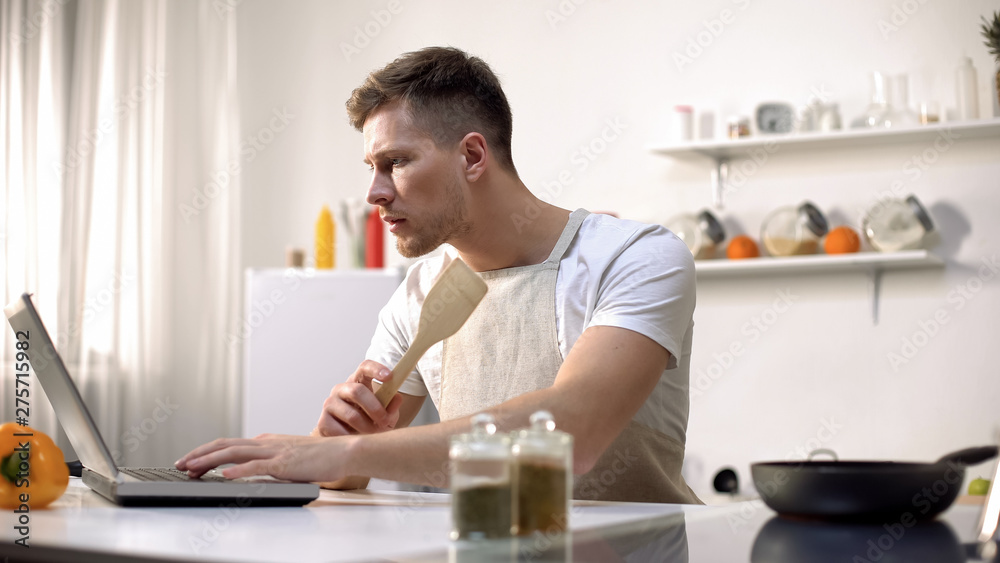 Male in apron searching for recipe in internet, online cooking tips in food blog