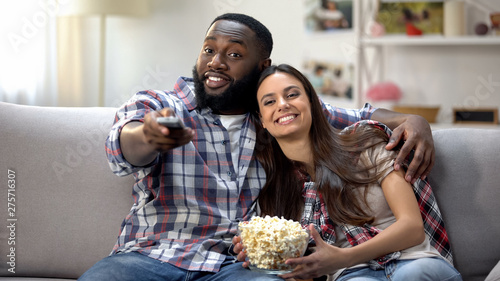 Multiracial family with pop corn switching channels, watching TV program at home