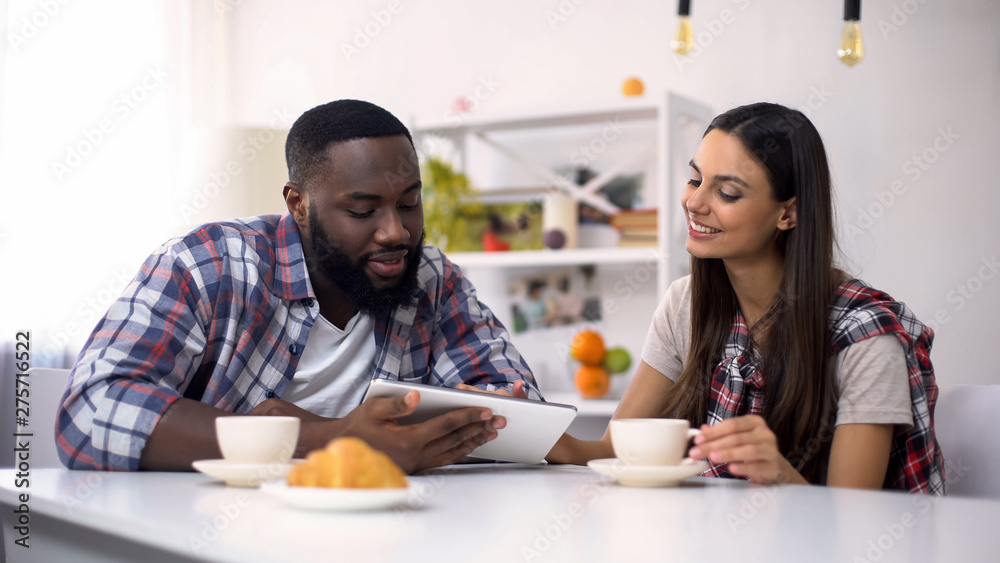Mixed-race family scrolling on tablet pc during breakfast, shopping online Mixed-race family scrolling on tablet pc during breakfast, shopping online