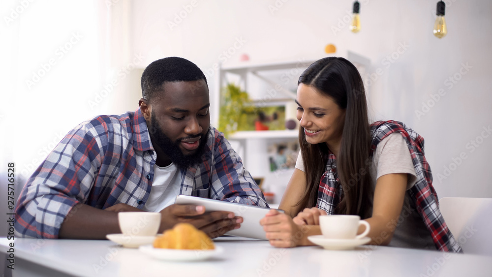 Young multiethnic couple drinking coffee and choosing vacation trip on tablet Young multiethnic couple drinking coffee and choosing vacation trip on tablet