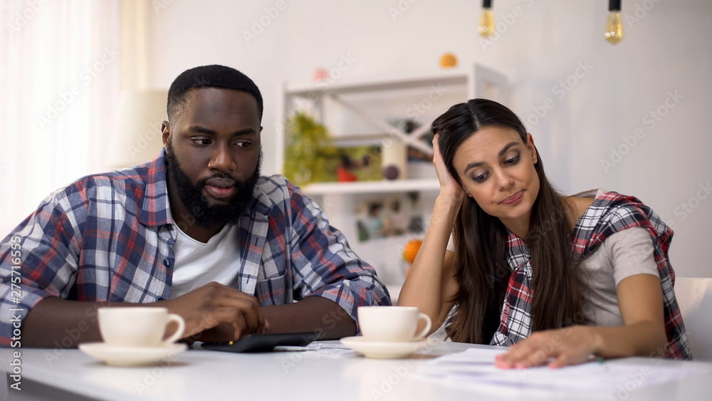 Fototapeta premium Multiracial family calculating budget, woman upset with unnecessary purchase