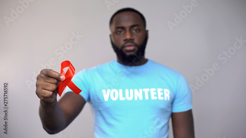 фотографія African-American volunteer showing red ribbon to camera, HIV/AIDS symbol
