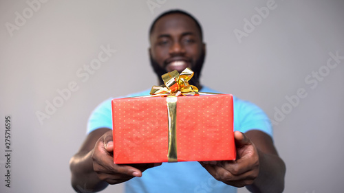 Photography Black male volunteer showing charity gift box at camera, present for poor kids