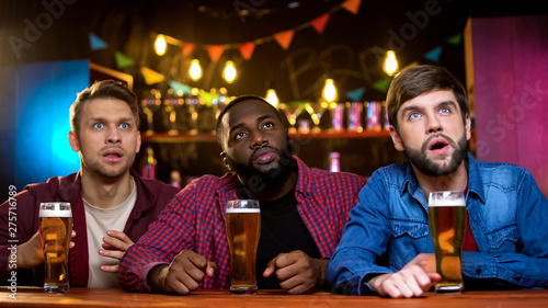 Excited multiracial friends watching sport channel sitting in beer pub  leisure