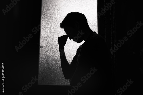 Tired, sad young man standing in a dark room.  photo
