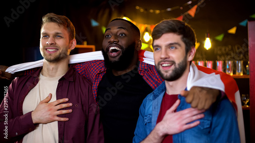 Fotografía Smiling multiethnic friends wrapped in english flag hugging, watching sport