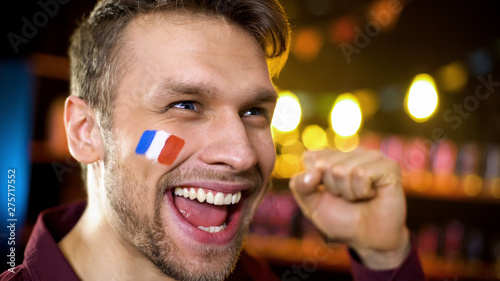 Joyful french fan with painted flag celebrating team victory  making yes gesture