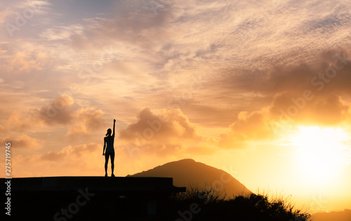 Strong woman with fist in the air standing on top a mountain. Triumph, victory and feeling determined. 