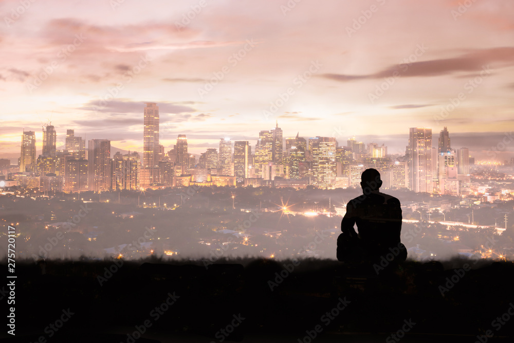 young thoughtful man in the watching the sunset over city skyline. 