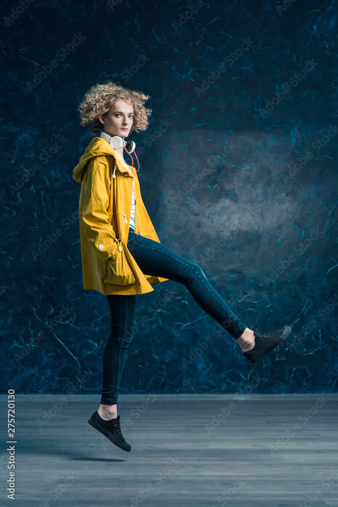 Naklejka premium Cute blond handsome guy in a yellow jacket and headphones jumping on dark blue background. Hang in fligh