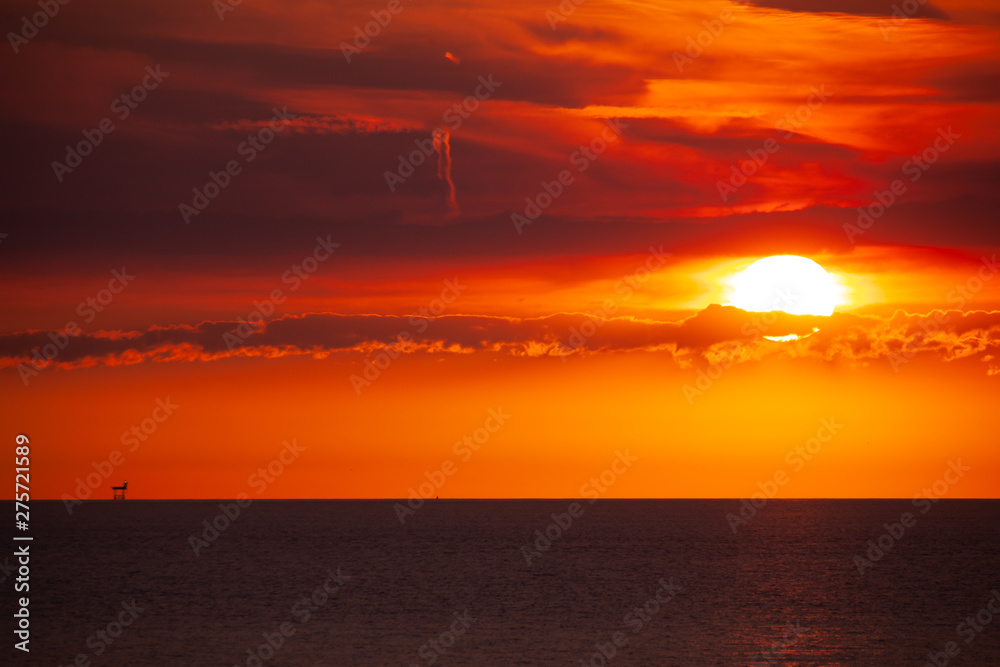 An oil platform in the sea in the distance on the horizon in the sunset.