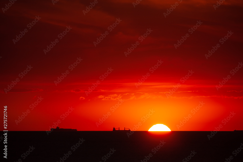 Boat traffic in the sunset on the North Sea. The sun touches the sea in the harbor entrance of Rotterdam.Silhouette of ships in front of glowing red background.