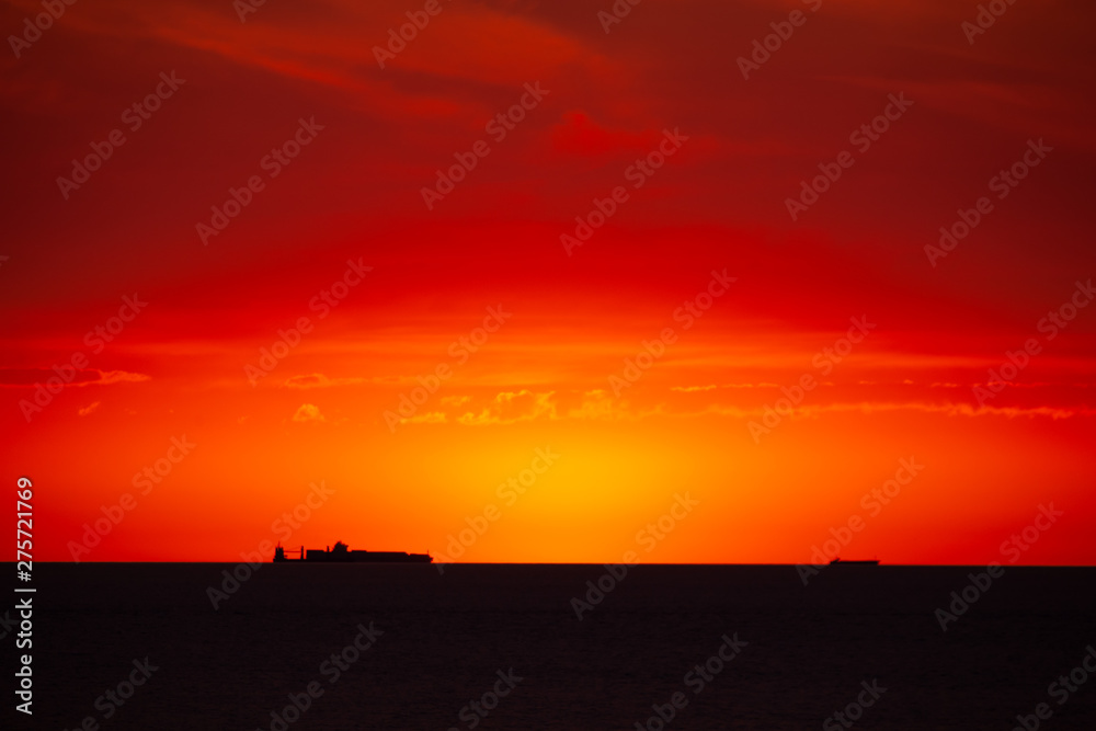 Cargo ship on the sea in sunset with cloud formations in red light. The sun has just disappeared. Cargo ship on the sea in sunset with cloud formations in red light. The sun has just disappeared.